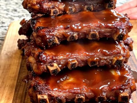 A close-up view of tender, slow-cooked General Tso spareribs stacked on a wooden board with a glossy sauce.