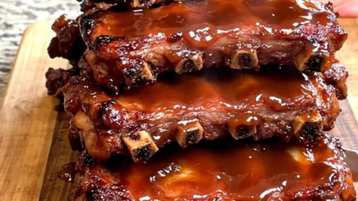 A close-up view of tender, slow-cooked General Tso spareribs stacked on a wooden board with a glossy sauce.