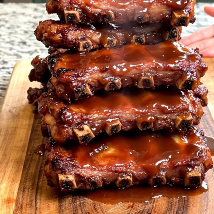 A close-up view of tender, slow-cooked General Tso spareribs stacked on a wooden board with a glossy sauce.