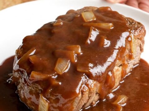 A close-up of tender, slow-cooked bone-in pork steaks covered in a rich, dark BBQ sauce with soft onions.