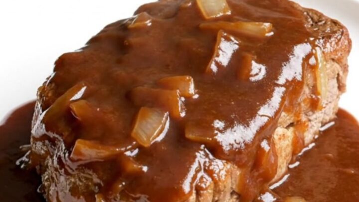 A close-up of tender, slow-cooked bone-in pork steaks covered in a rich, dark BBQ sauce with soft onions.