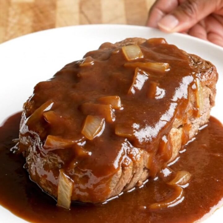 A close-up of tender, slow-cooked bone-in pork steaks covered in a rich, dark BBQ sauce with soft onions.