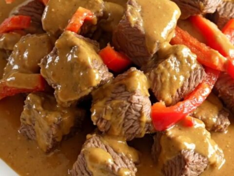 A close-up of slow cooker Thai peanut beef served on a white plate with visible peppers and creamy sauce.