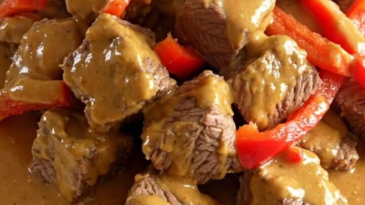 A close-up of slow cooker Thai peanut beef served on a white plate with visible peppers and creamy sauce.