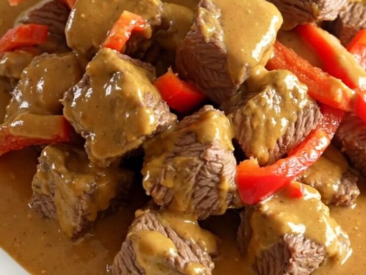 A close-up of slow cooker Thai peanut beef served on a white plate with visible peppers and creamy sauce.