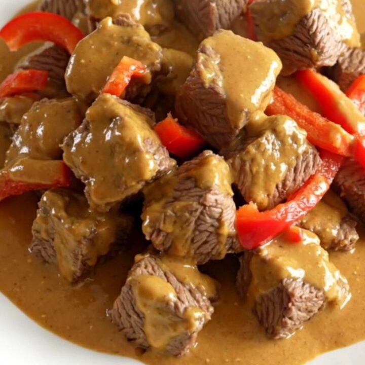 A close-up of slow cooker Thai peanut beef served on a white plate with visible peppers and creamy sauce.