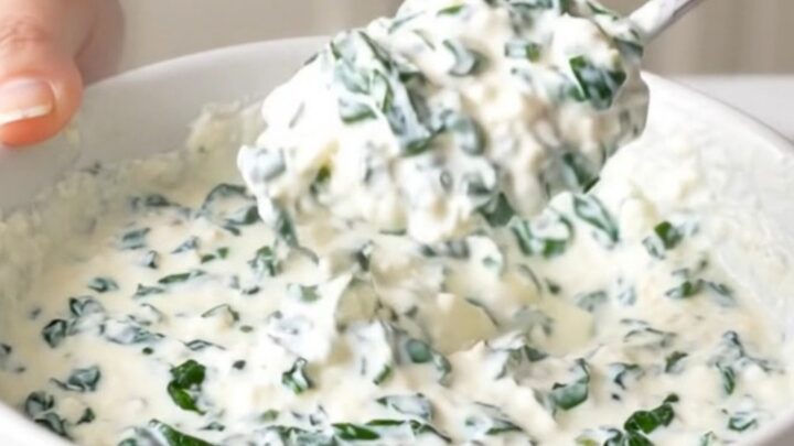 A close-up view of creamy white queso dip in a black slow cooker, topped with spinach and green chiles.