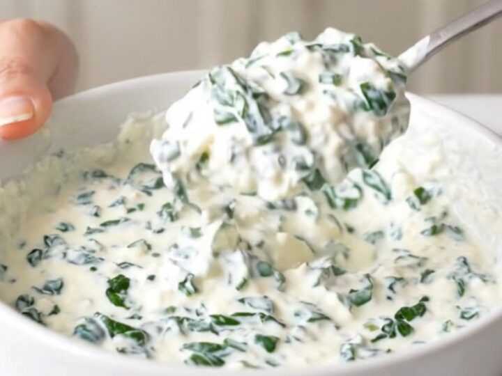 A close-up view of creamy white queso dip in a black slow cooker, topped with spinach and green chiles.