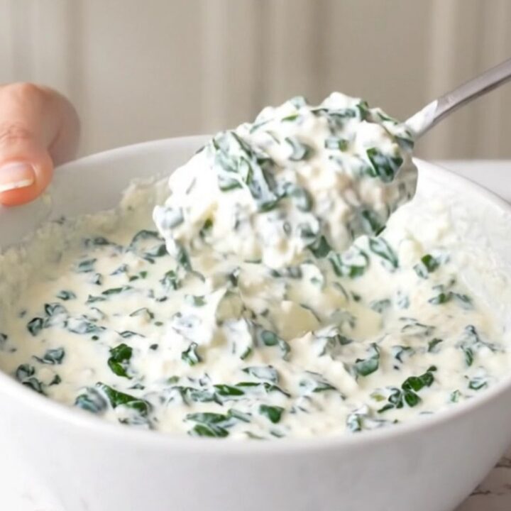 A close-up view of creamy white queso dip in a black slow cooker, topped with spinach and green chiles.