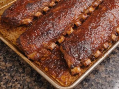 Three racks of glistening, caramelized oven-baked barbecue ribs resting on a foil-lined baking sheet.