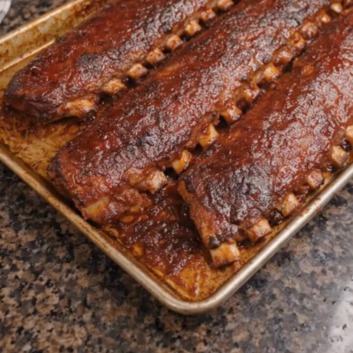 Three racks of glistening, caramelized oven-baked barbecue ribs resting on a foil-lined baking sheet.