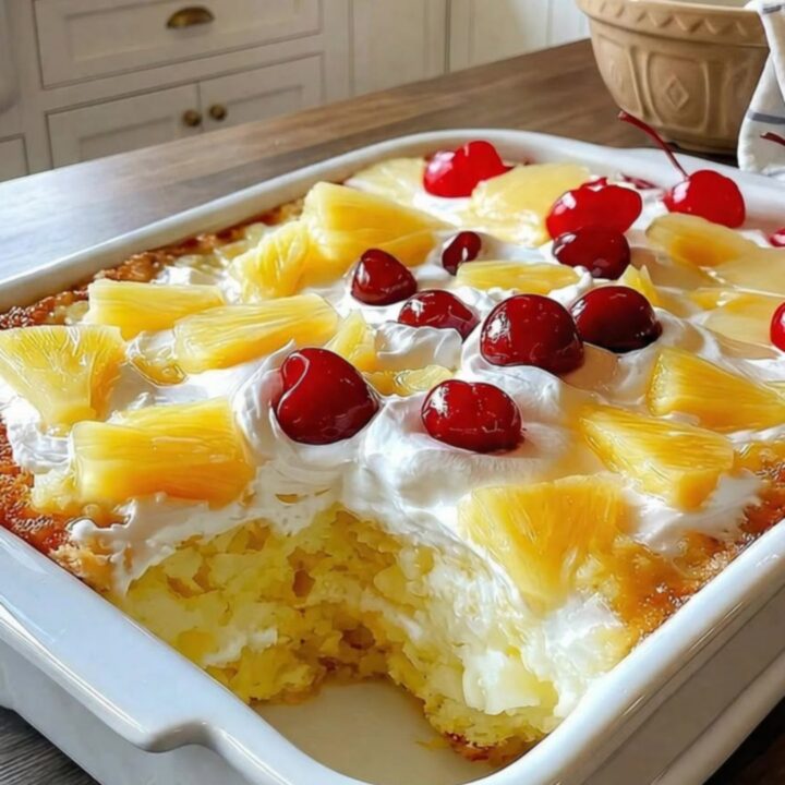 A close-up of a slice of yellow cake topped with whipped cream, pineapple, and a cherry.