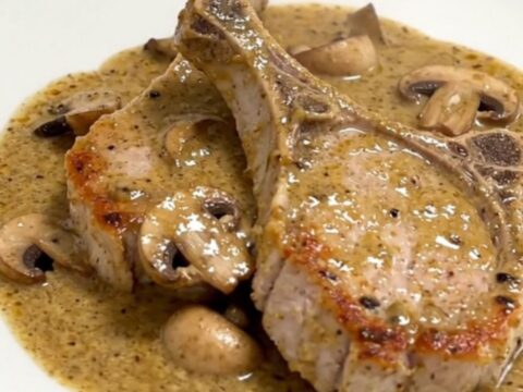 Five raw boneless pork chops fanned out in a slow cooker insert with mushrooms and cream sauce.