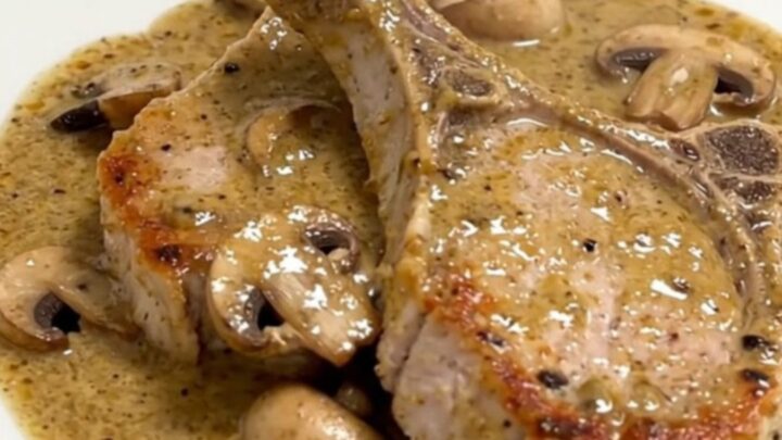 Five raw boneless pork chops fanned out in a slow cooker insert with mushrooms and cream sauce.