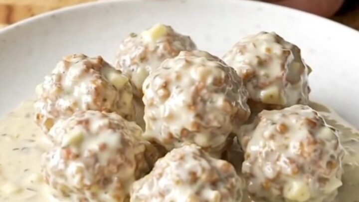 A close-up shot of creamy alfredo meatballs in a slow cooker, being scooped with a spoon.