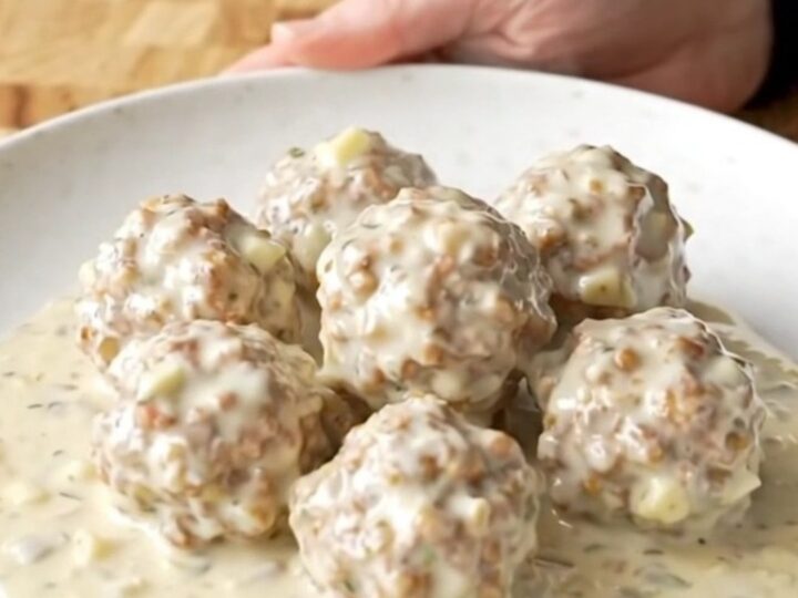 A close-up shot of creamy alfredo meatballs in a slow cooker, being scooped with a spoon.