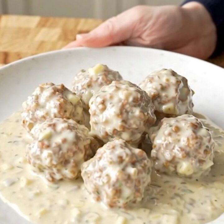 A close-up shot of creamy alfredo meatballs in a slow cooker, being scooped with a spoon.
