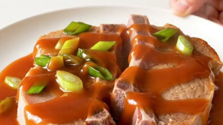 A close-up of tender, braised pork chops in a slow cooker, glazed with a vibrant red-orange honey sriracha sauce.