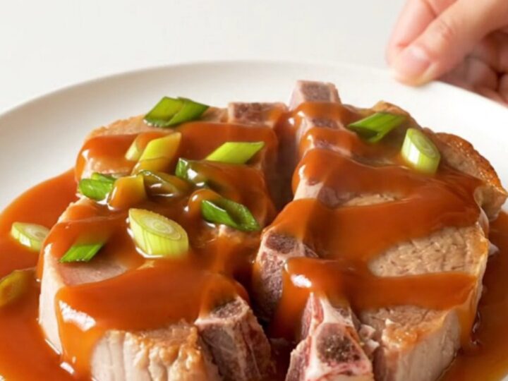 A close-up of tender, braised pork chops in a slow cooker, glazed with a vibrant red-orange honey sriracha sauce.