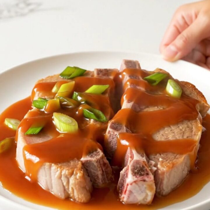 A close-up of tender, braised pork chops in a slow cooker, glazed with a vibrant red-orange honey sriracha sauce.