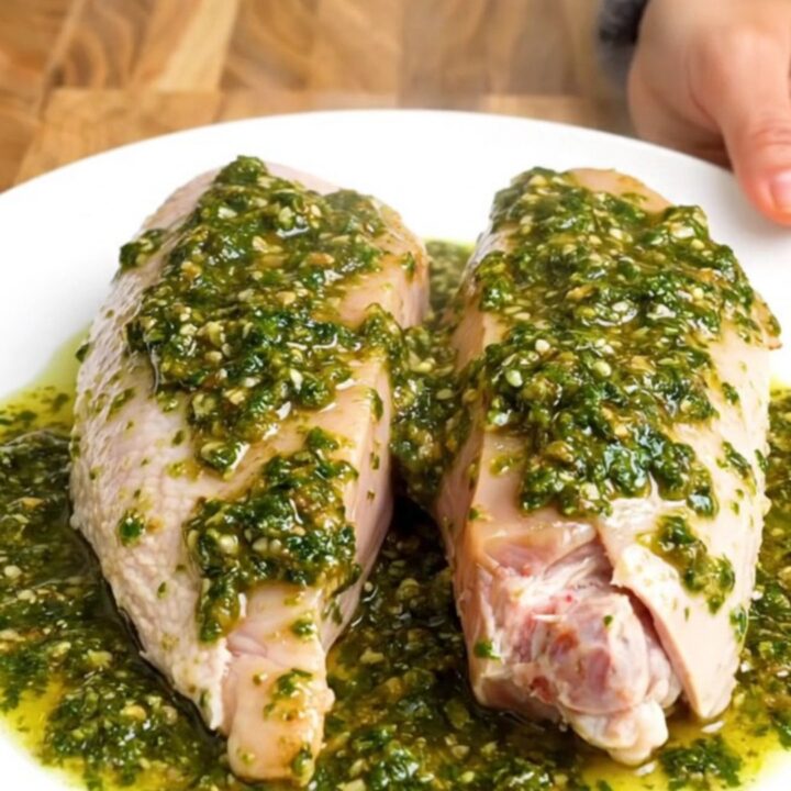 A stainless steel slow cooker filled with raw turkey tenderloins, sliced red onions, and fresh chimichurri sauce.