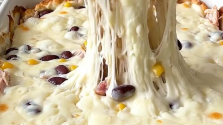 A bubbling, cheesy Cowboy Queso Bake in a rectangular ceramic dish, topped with black beans and corn.