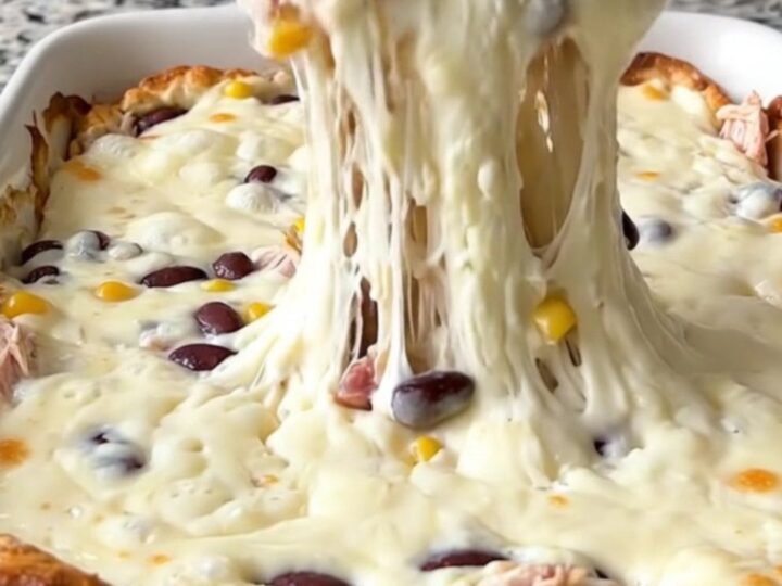 A bubbling, cheesy Cowboy Queso Bake in a rectangular ceramic dish, topped with black beans and corn.