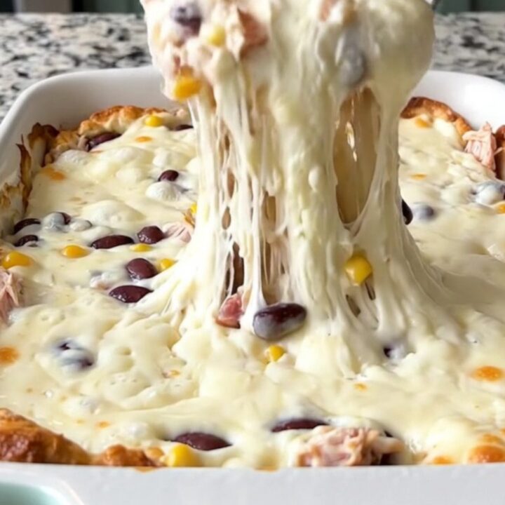 A bubbling, cheesy Cowboy Queso Bake in a rectangular ceramic dish, topped with black beans and corn.