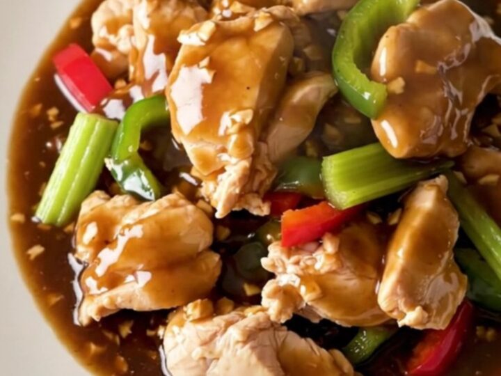 A high-angle shot of tender chicken chunks in a savory garlic sauce with colorful bell peppers and celery.