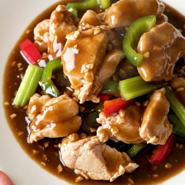 A high-angle shot of tender chicken chunks in a savory garlic sauce with colorful bell peppers and celery.