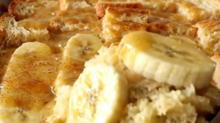 A top-down view of a rectangular baking dish filled with golden-brown bread pudding and soft banana slices.