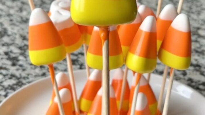 A dozen candy corn marshmallow pops on a baking sheet, featuring bright orange coating and festive candy corn sprinkles.