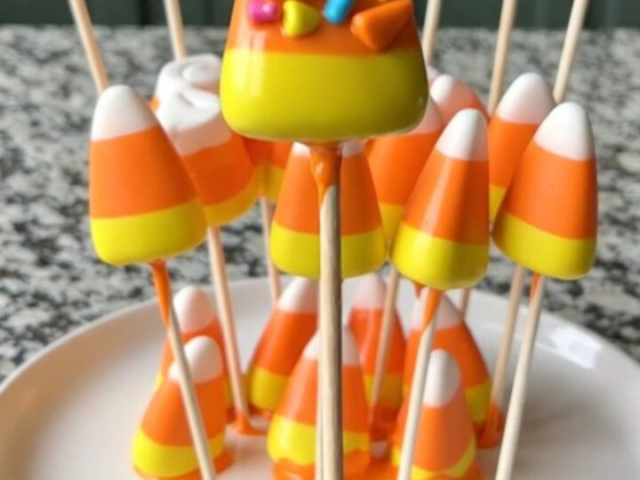 A dozen candy corn marshmallow pops on a baking sheet, featuring bright orange coating and festive candy corn sprinkles.