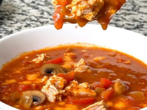 A steaming bowl of cheesy ground turkey pizza soup with visible mushrooms and peppers.
