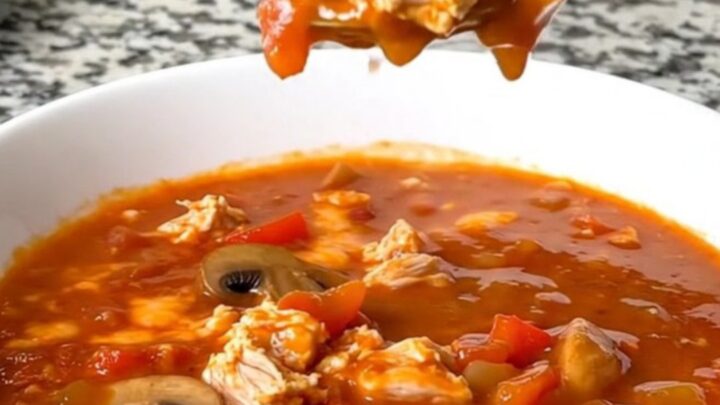 A steaming bowl of cheesy ground turkey pizza soup with visible mushrooms and peppers.
