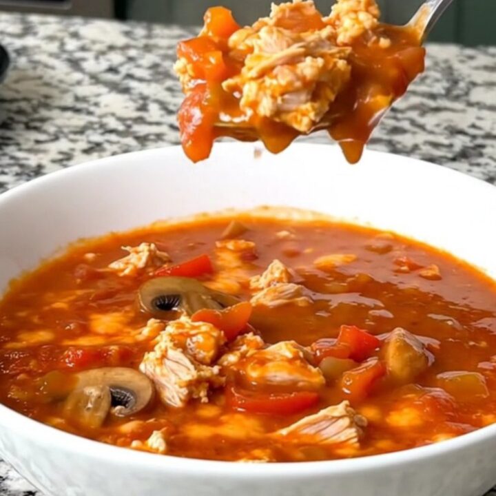 A steaming bowl of cheesy ground turkey pizza soup with visible mushrooms and peppers.