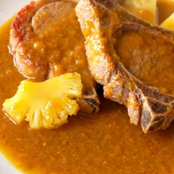 Five succulent, braised pork chops coated in a glossy orange pineapple habanero sauce on a white plate.