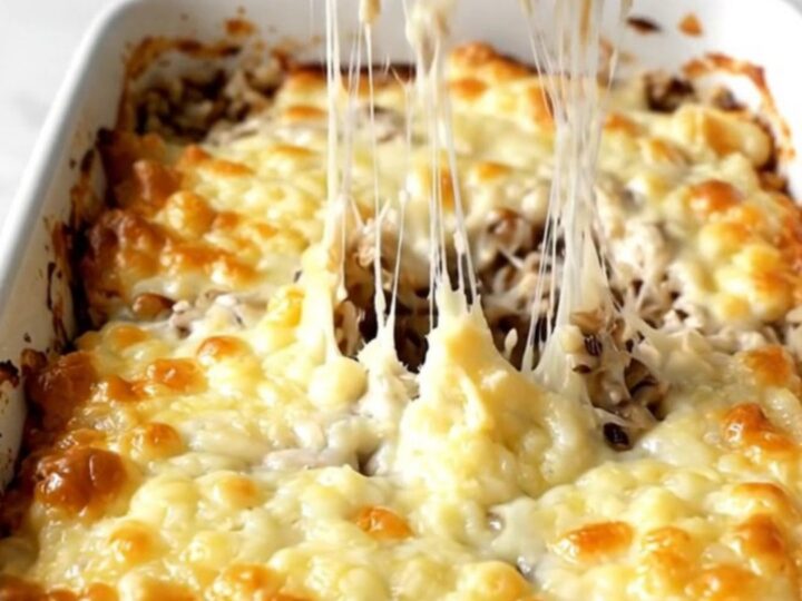 A top-down view of a creamy mushroom and wild rice bake topped with melted Gruyère cheese in a ceramic dish.