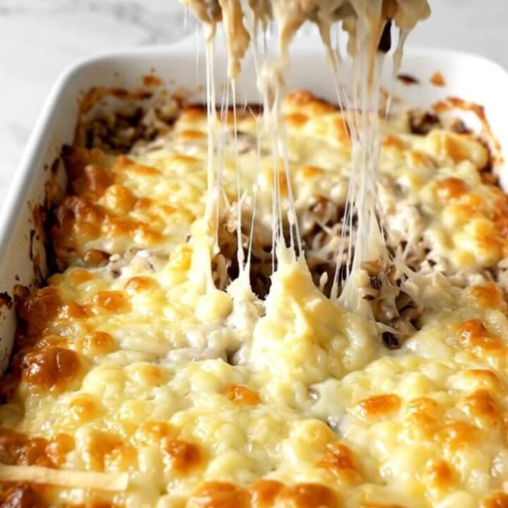 A top-down view of a creamy mushroom and wild rice bake topped with melted Gruyère cheese in a ceramic dish.