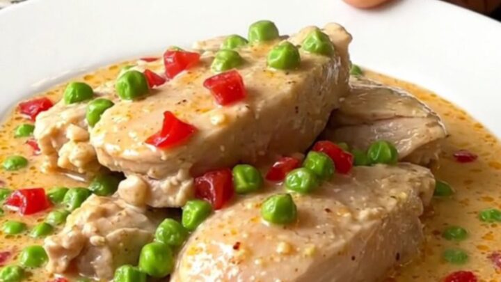 A close-up view of creamy Chicken a la King in a slow cooker, featuring chicken chunks, peas, and pimentos.
