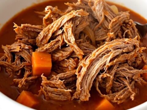 A close-up of tender, shredded beef in a rich tomato sauce with visible pieces of carrot and onion.