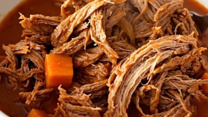 A close-up of tender, shredded beef in a rich tomato sauce with visible pieces of carrot and onion.