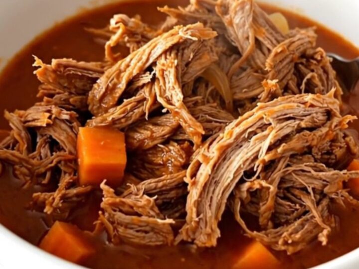 A close-up of tender, shredded beef in a rich tomato sauce with visible pieces of carrot and onion.