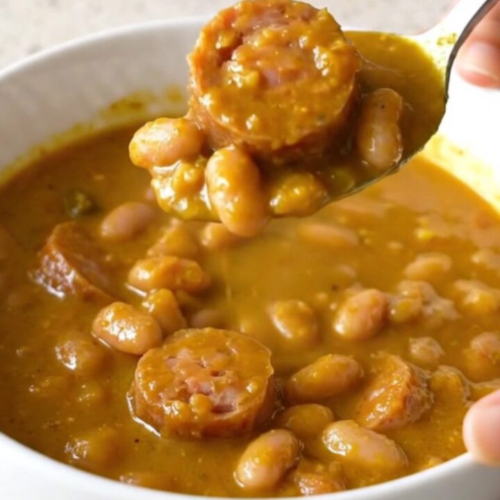 A slow cooker filled with pumpkin sausage stew featuring Italian sausage rounds and white beans.