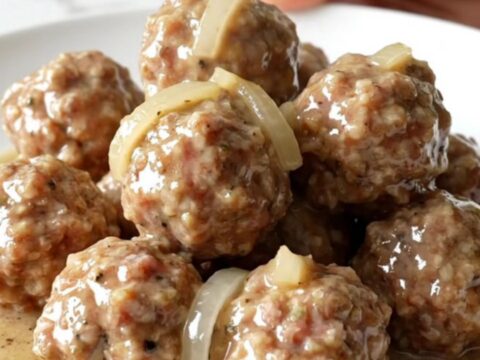 A slow cooker filled with turkey meatballs, sliced onions, and creamy country gravy on a white speckled countertop.
