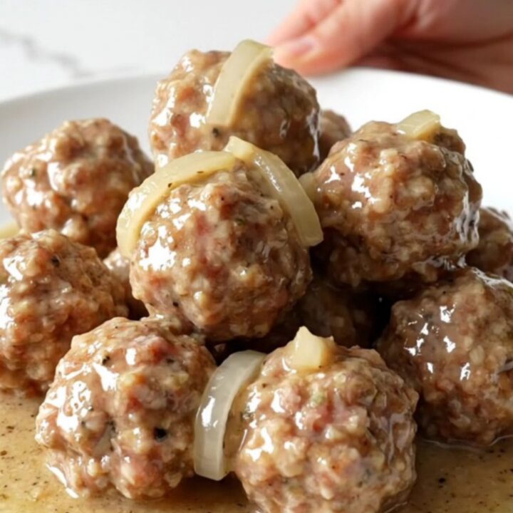 A slow cooker filled with turkey meatballs, sliced onions, and creamy country gravy on a white speckled countertop.