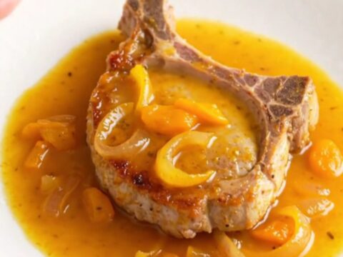 A succulent pork chop covered in a glossy apricot and onion sauce on a white plate.