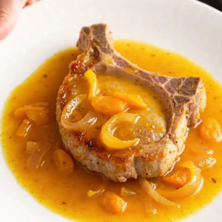 A succulent pork chop covered in a glossy apricot and onion sauce on a white plate.