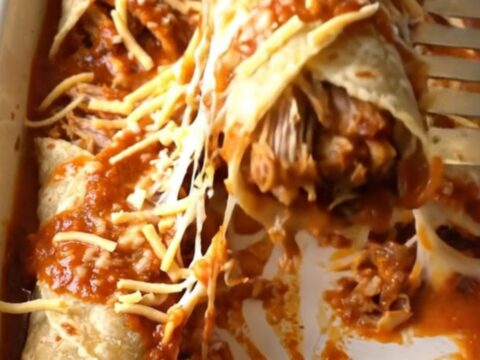 A close-up of a golden, cheesy shredded pork enchilada bake in a white rectangular dish.
