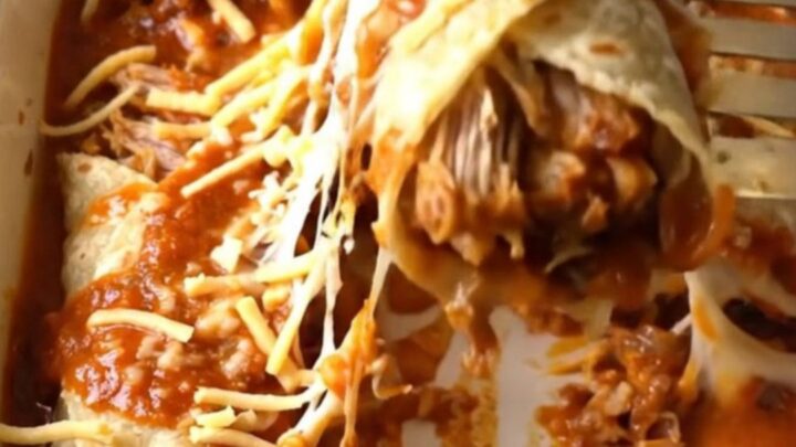 A close-up of a golden, cheesy shredded pork enchilada bake in a white rectangular dish.